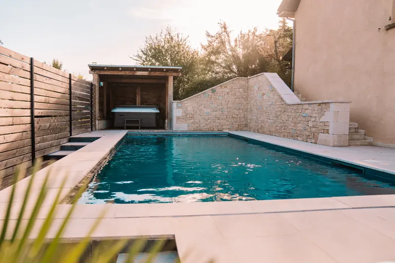Piscine et spa sous abri – Margelles en pierre claire, mur en pierre sèche et spa sous abri bois.
