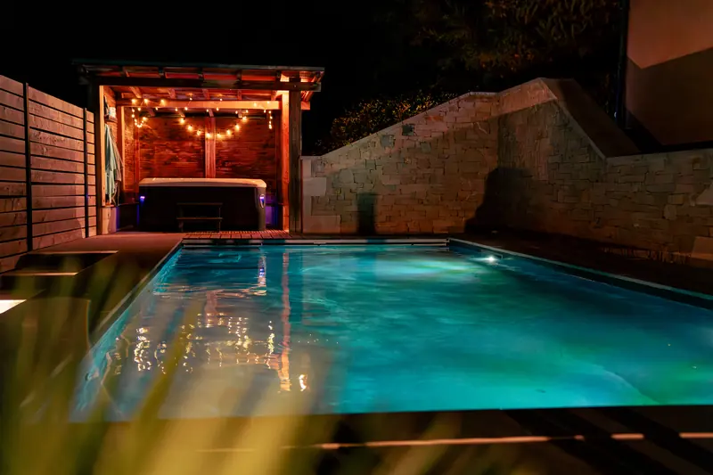 La même piscine, de nuit – Éclairage LED subaquatique et spa sous abri illuminé.