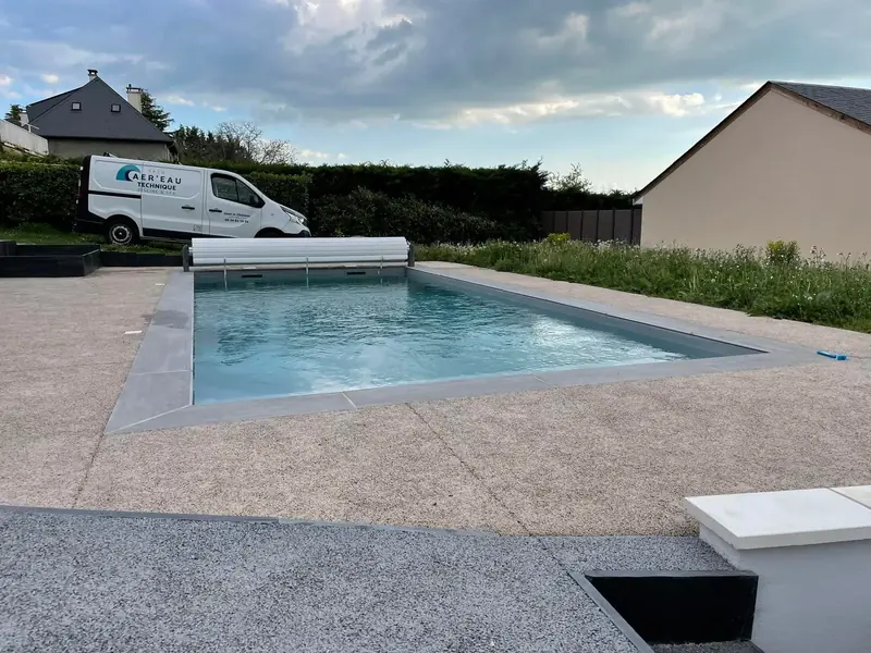 Piscine avec volet roulant – Construction avec volet de sécurité et plage minérale.