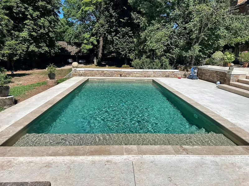 Rénovation de piscine – Margelles en pierre et plage immergée sur toute la largeur.