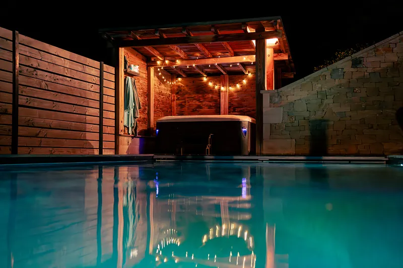 Spa sous abri, de nuit – Spa installé sous un abri bois éclairé, au bord de la piscine.